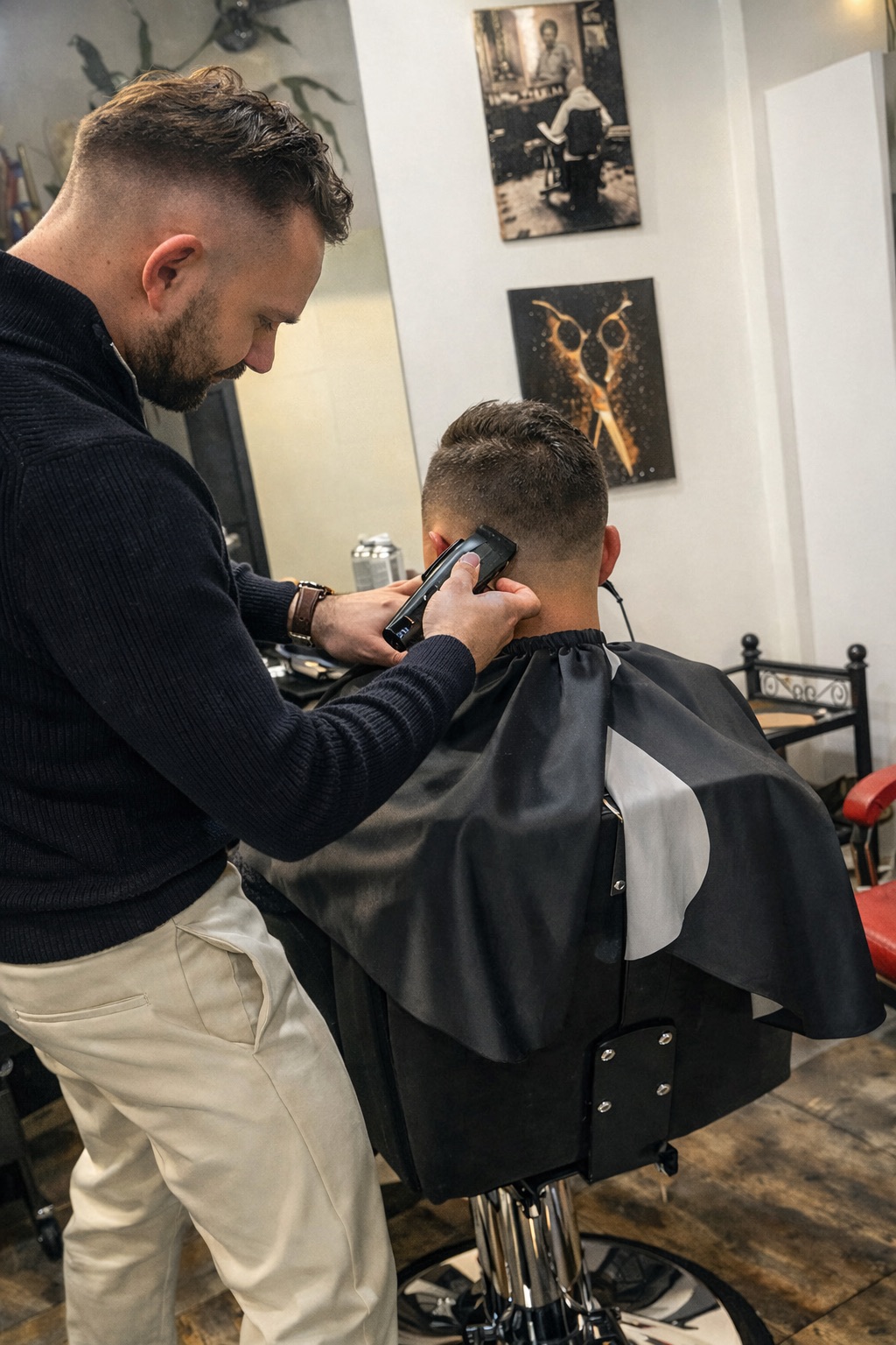 Barber przycina włosy mężczyzny maszynką, tworząc płynne przejście fade w tylnej części głowy w salonie barberskim