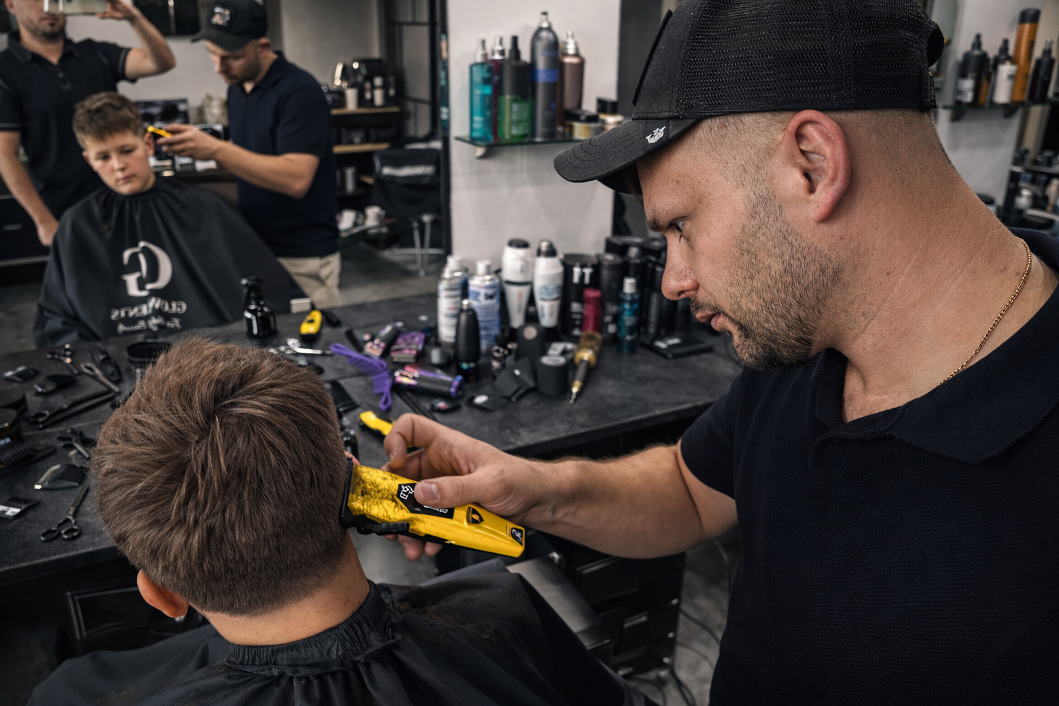 Barber przycina włosy chłopca maszynką, wykonując precyzyjne cieniowanie w tylnej części głowy w salonie fryzjerskim