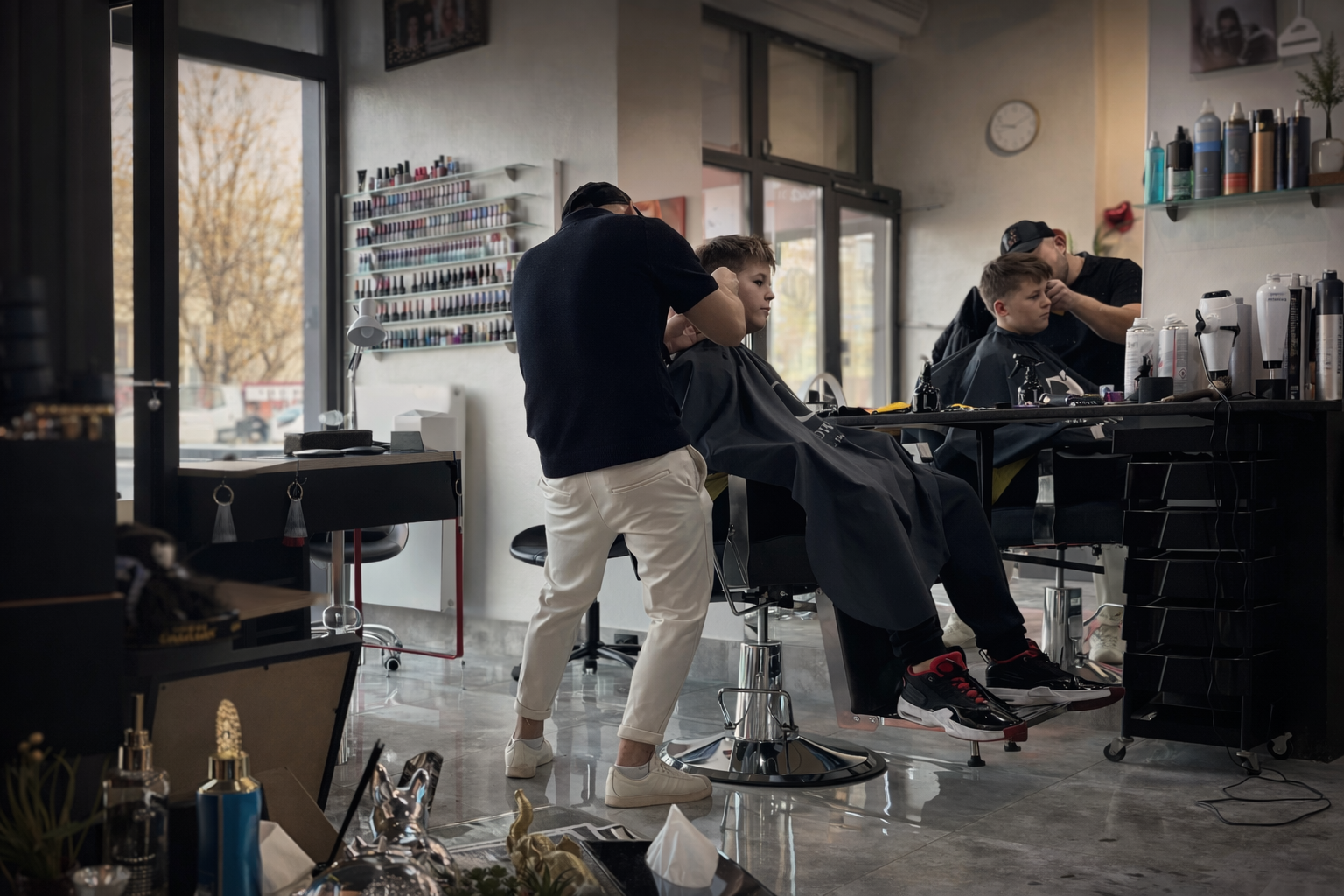 Barber strzyże włosy chłopca na fotelu fryzjerskim, podczas gdy inni klienci są obsługiwani przy stanowiskach w tle