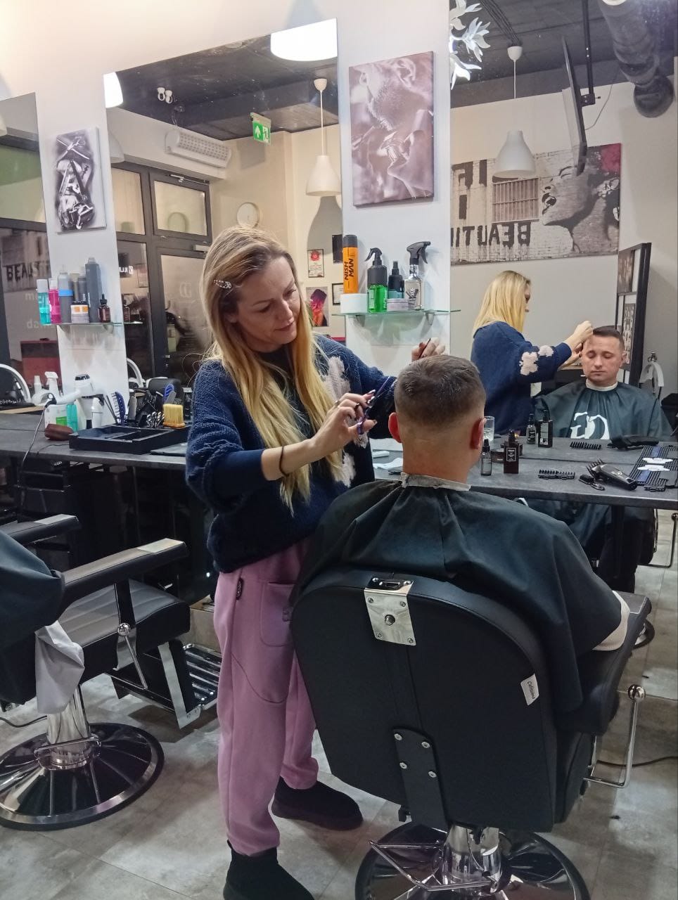 Fryzjerka przycina włosy mężczyzny maszynką przy stanowisku z lustrem, wykonując dokładne strzyżenie w salonie fryzjerskim