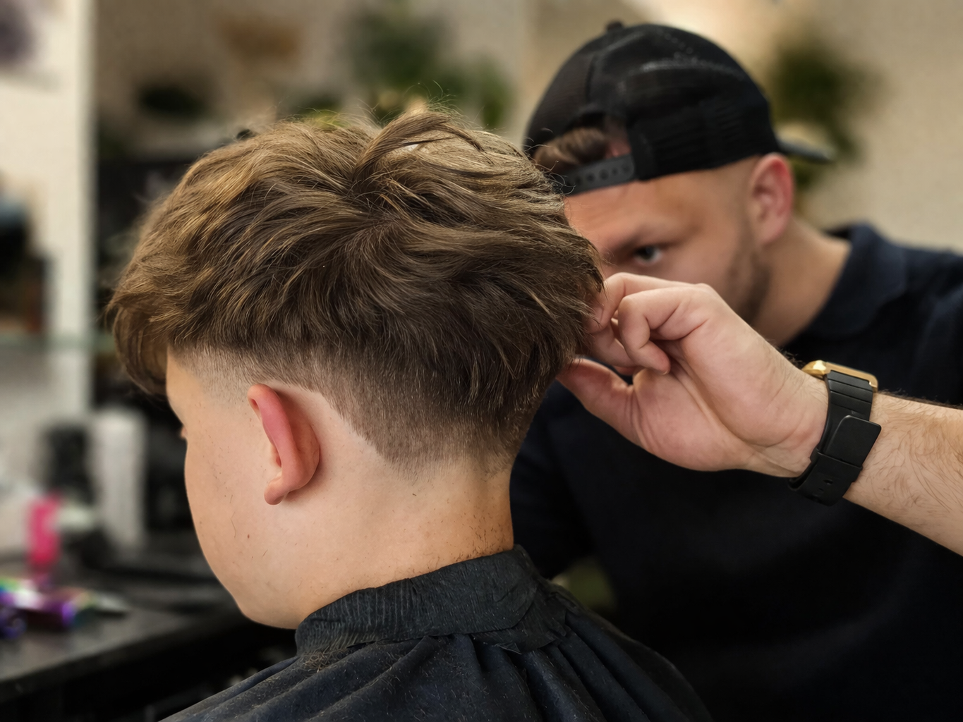 Barber przycina włosy chłopca nożyczkami, dopracowując kształt fryzury i wykończenie przy karku w salonie