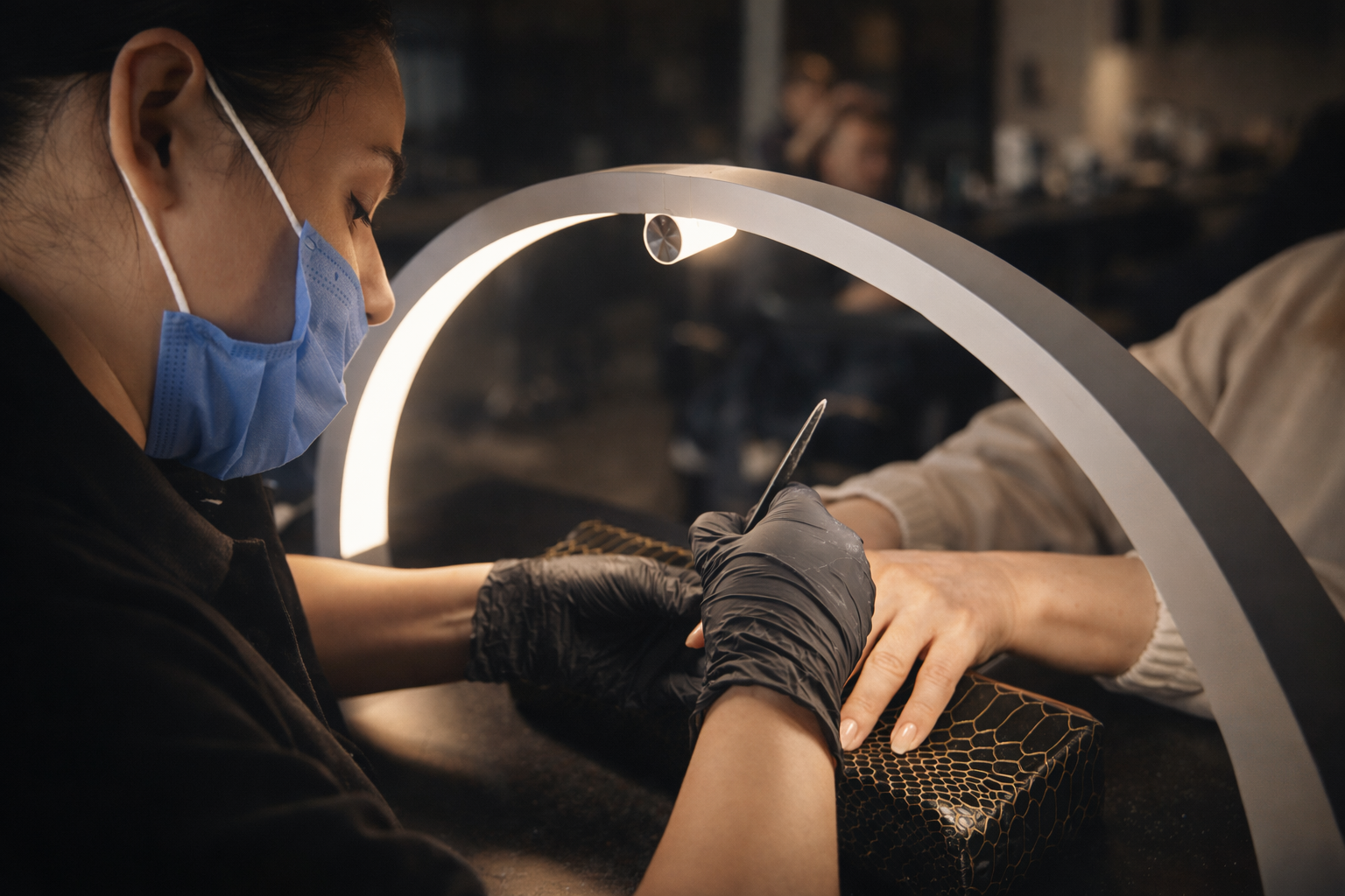 Stylistka wykonuje manicure klientce pod lampą, precyzyjnie opracowując paznokcie w profesjonalnym salonie kosmetycznym