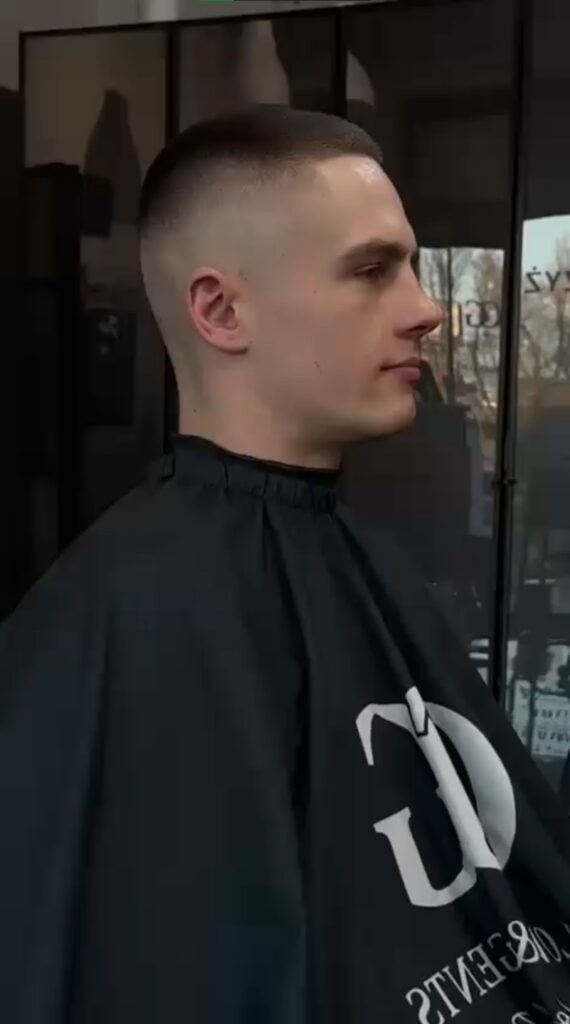 Mężczyzna po strzyżeniu z krótką fryzurą typu fade, siedzący w fotelu w salonie fryzjerskim