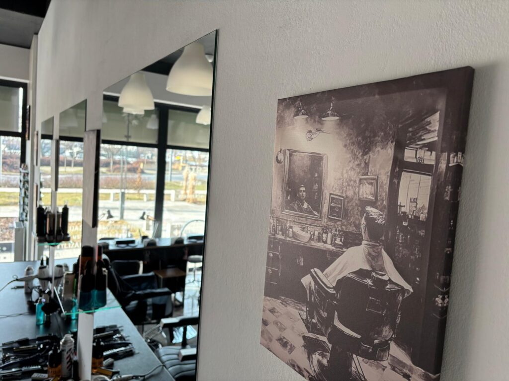 Fragment wnętrza salonu fryzjerskiego z lustrem i stanowiskiem pracy oraz obrazem przedstawiającym klasyczny barber shop na ścianie