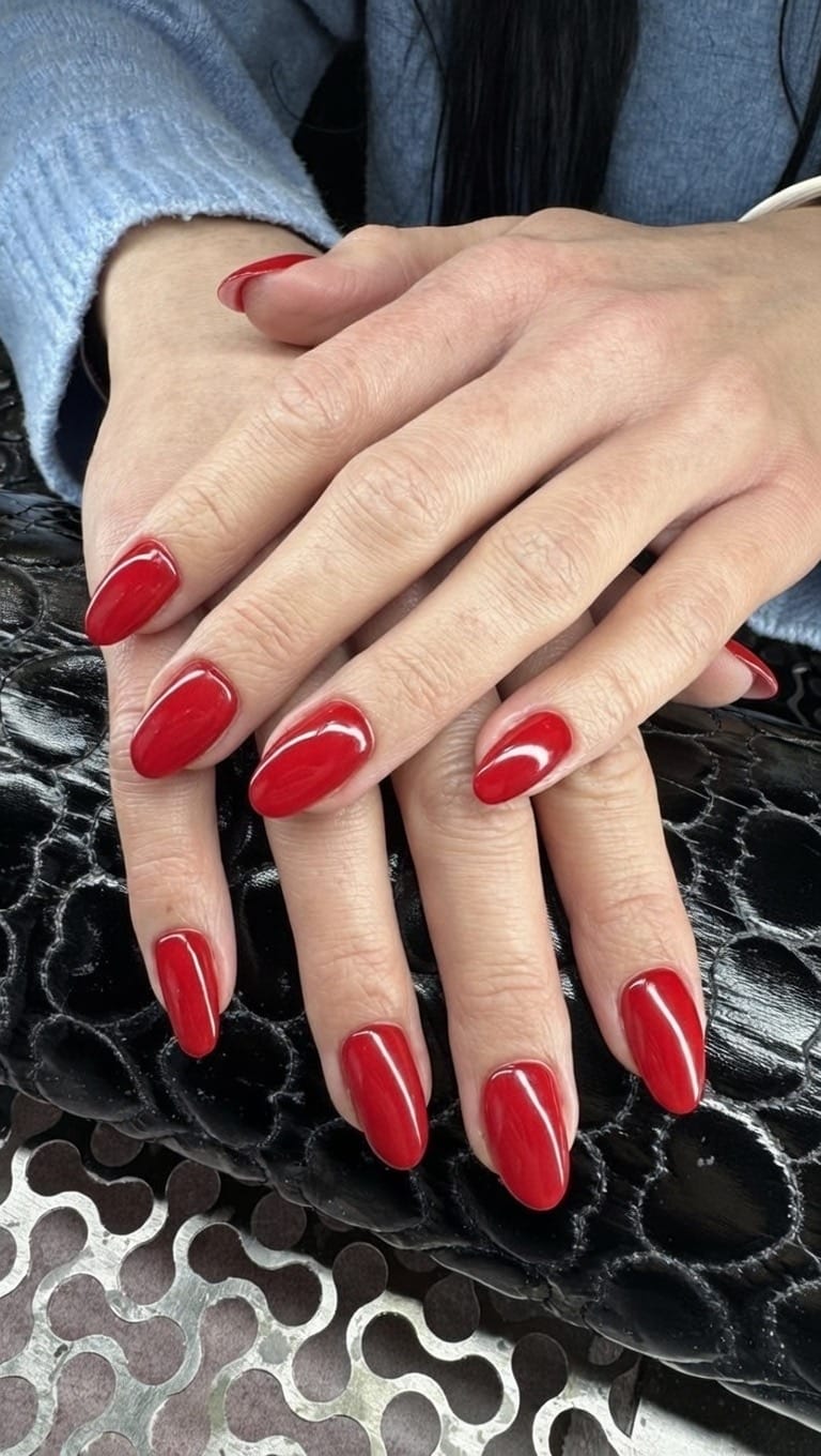 Dłonie z paznokciami w intensywnym czerwonym kolorze o migdałowym kształcie, prezentujące elegancki i zadbany manicure