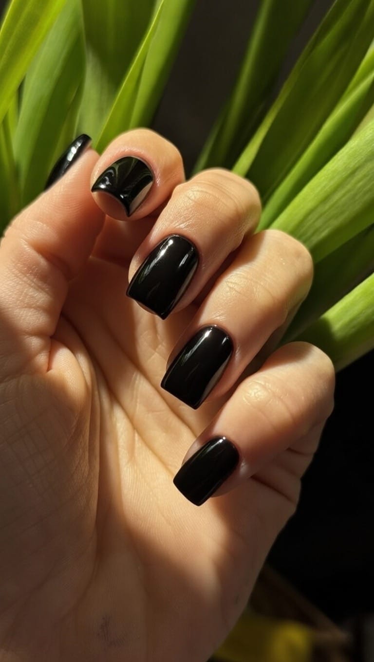 Dłoń z paznokciami pomalowanymi na czarny kolor o wysokim połysku, prezentująca elegancki i minimalistyczny manicure