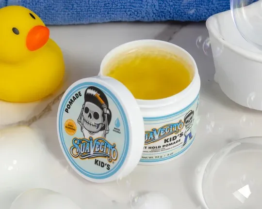 Otwarta pomada Suavecito Kid’s do stylizacji włosów dzieci z widoczną żelową konsystencją, ustawiona na blacie obok akcesoriów łazienkowych