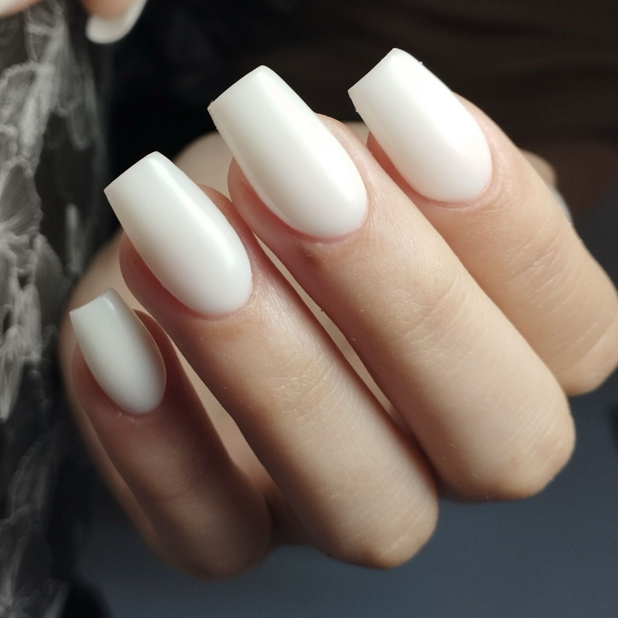 Dłoń z długimi paznokciami w białym, matowym wykończeniu o prostym kształcie, prezentująca minimalistyczny manicure