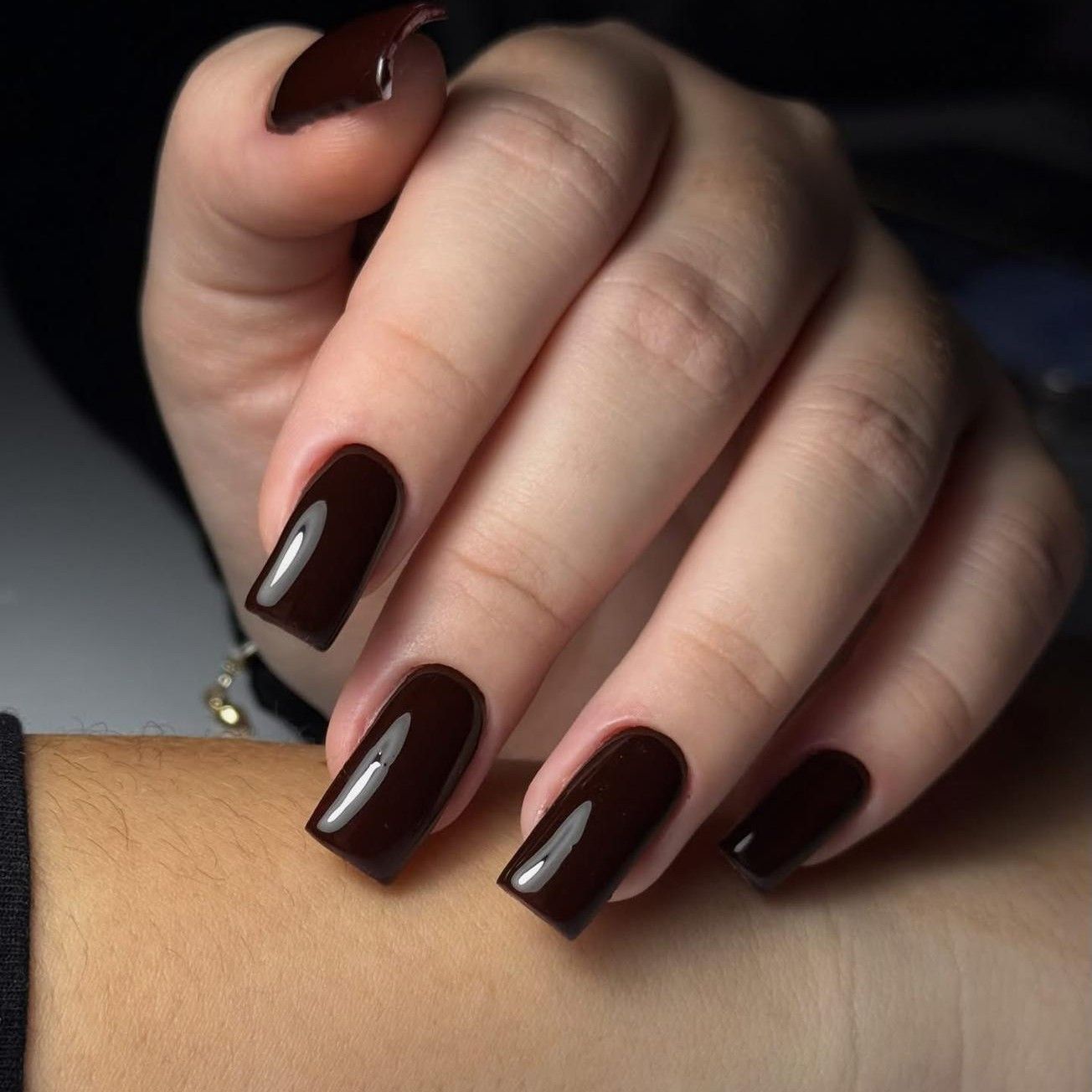 Dłoń z paznokciami w głębokim brązowym kolorze o wysokim połysku, prezentująca elegancki i nowoczesny manicure