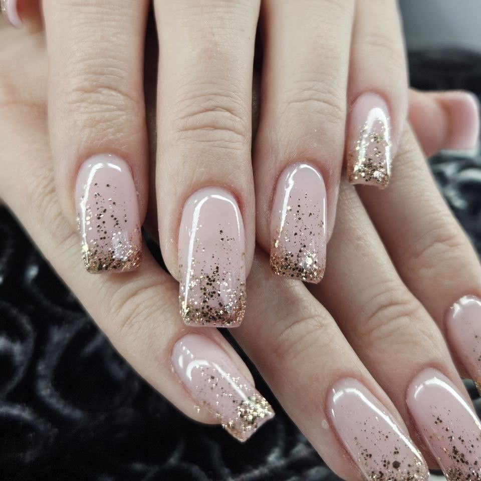 Dłonie z paznokciami w odcieniu nude ozdobionymi złotym brokatem na końcówkach, tworzące elegancki i subtelny manicure