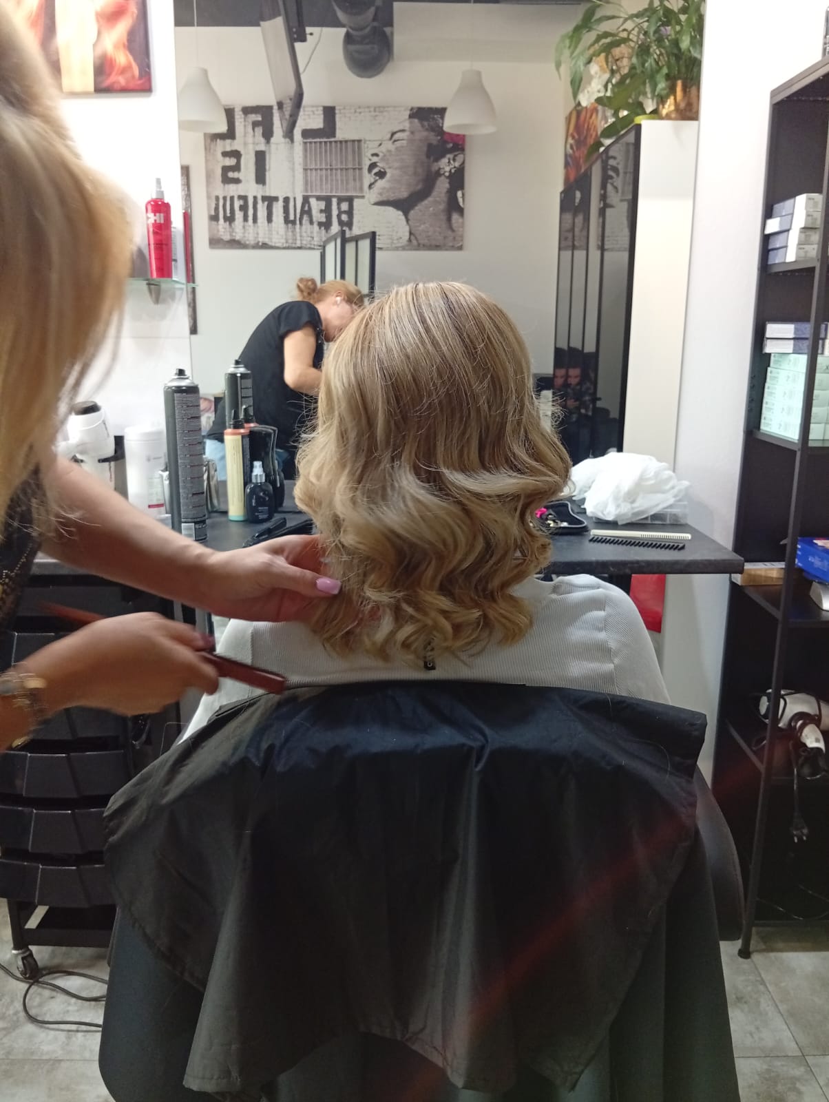 Średniej długości blond włosy z miękkimi falami podczas końcowej stylizacji w salonie fryzjerskim.