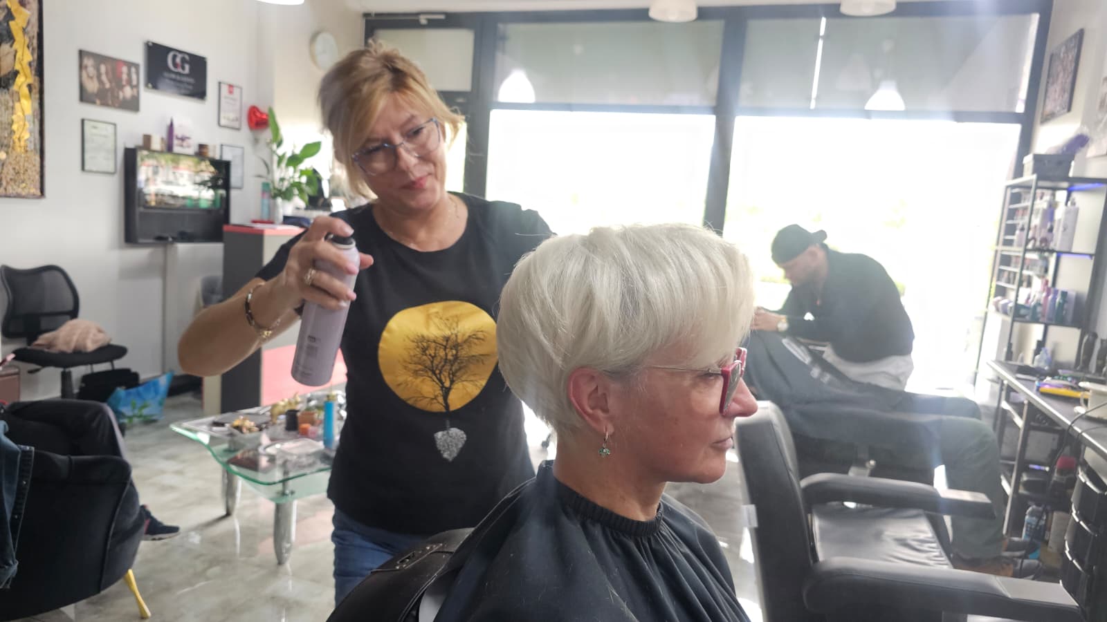 Fryzjerka utrwalająca krótką platynową fryzurę podczas końcowej stylizacji w salonie fryzjerskim.