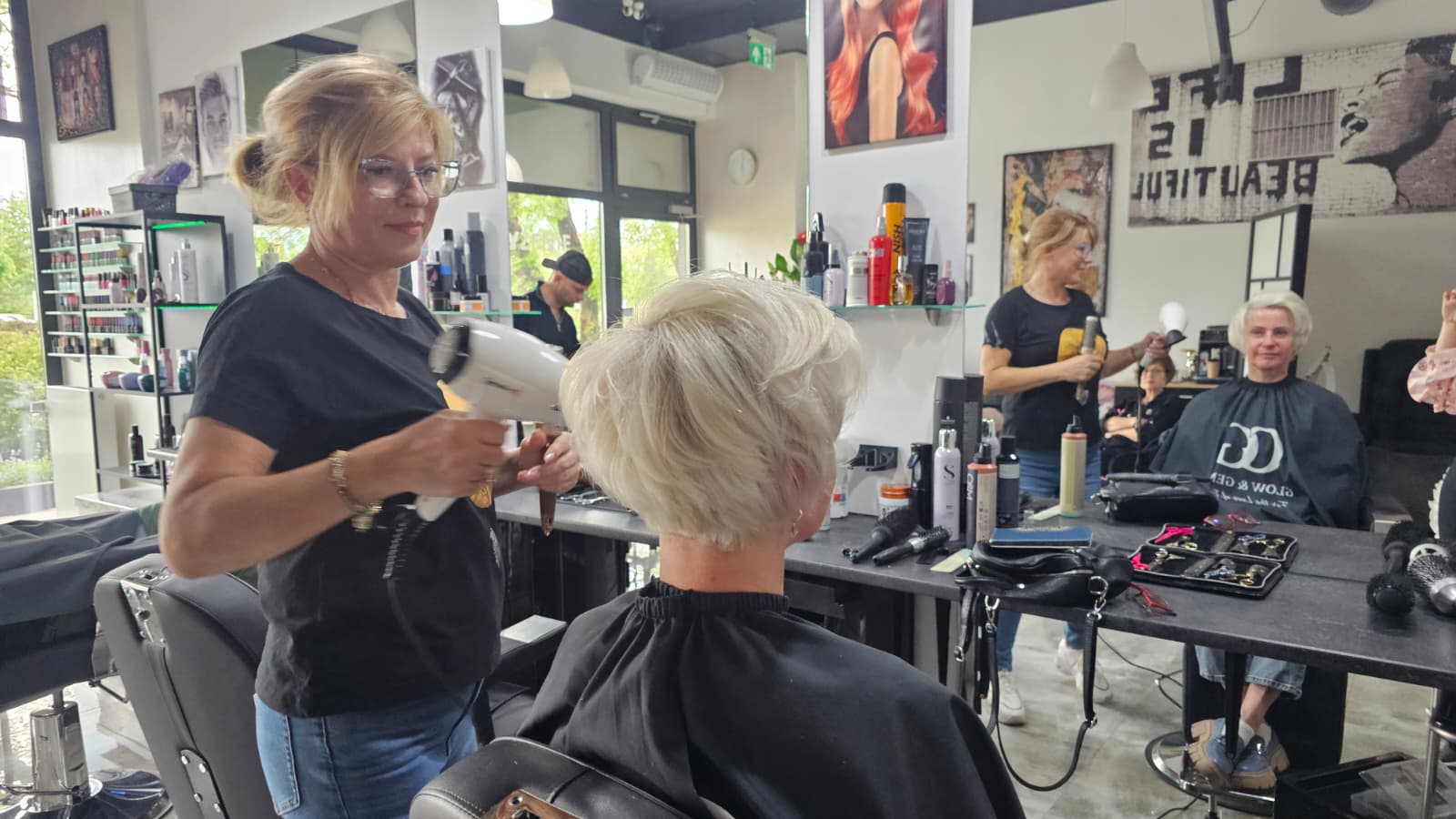 Fryzjerka modelująca krótką blond fryzurę podczas stylizacji w nowoczesnym salonie fryzjerskim.
