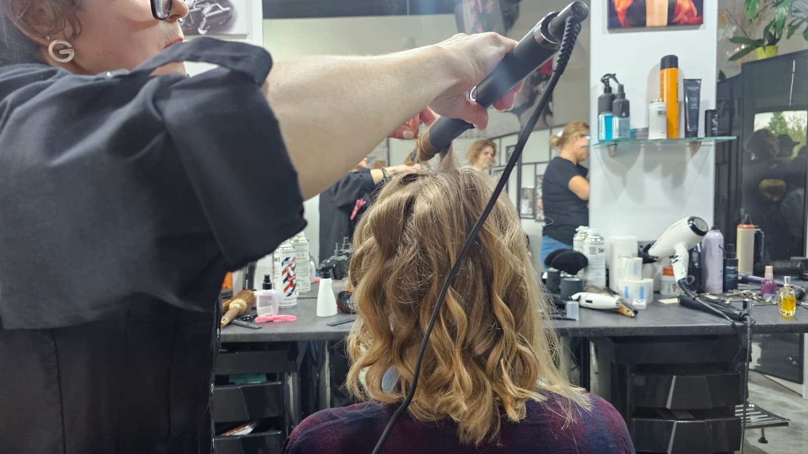 Fryzjerka stylizująca włosy lokówką podczas tworzenia miękkich fal w salonie fryzjerskim.