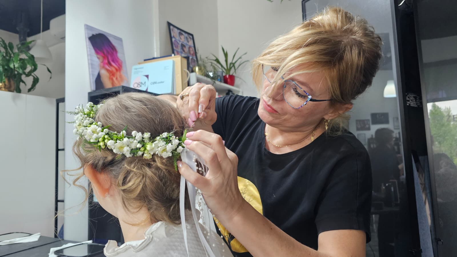Fryzjerka wykonująca eleganckie upięcie komunijne z delikatnym wiankiem z białych kwiatów.