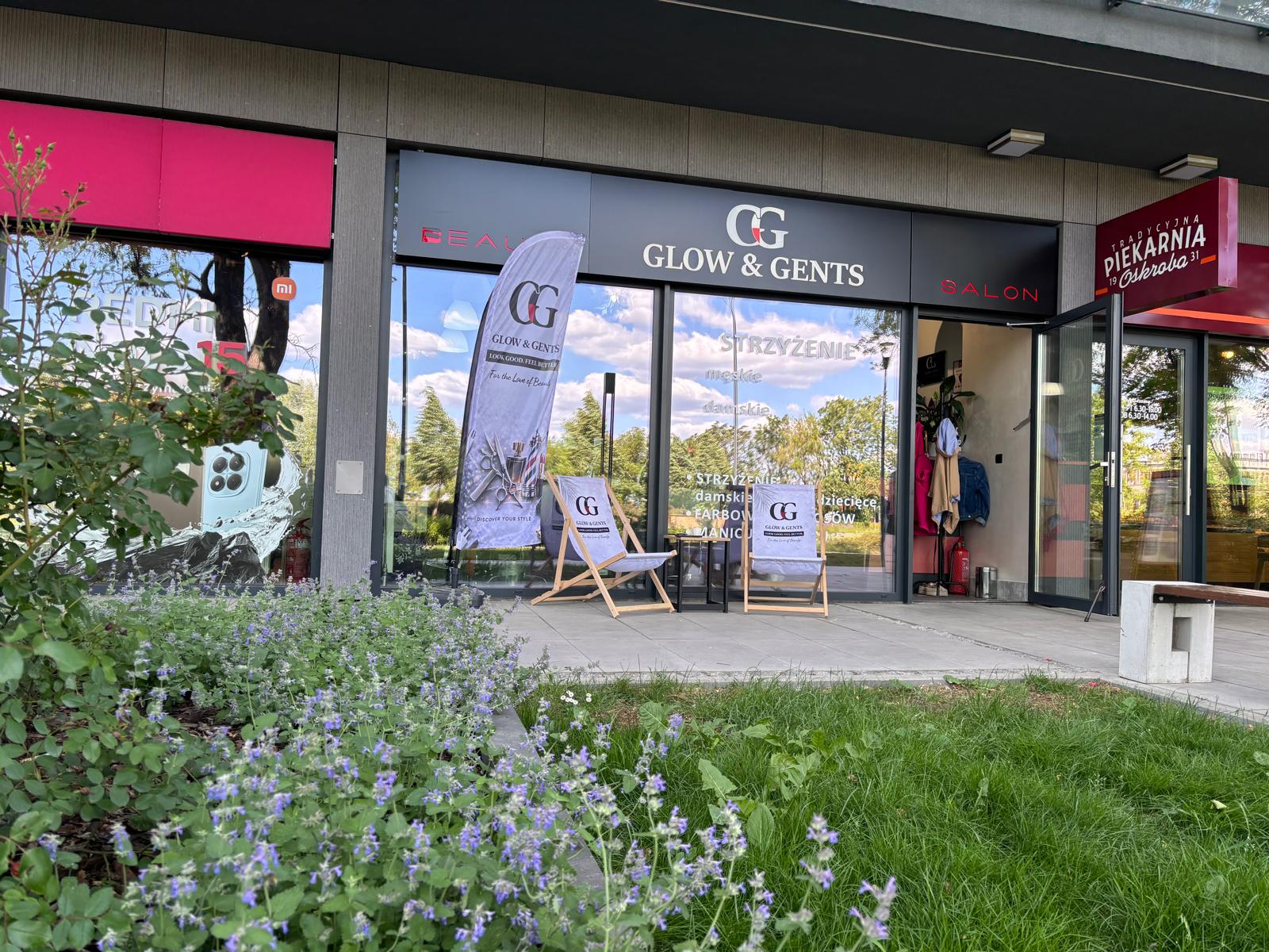 Wejście do salonu fryzjerskiego Glow & Gents z witryną, strefą relaksu i widokiem na ogródek przed lokalem.