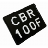 Czarna tablica rejestracyjna do motocykla z białym oznaczeniem „CBR 100F”, pokazana pod kątem.