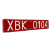 Czerwona tablica rejestracyjna z białym napisem „XBK 0104”, pokazana pod kątem.